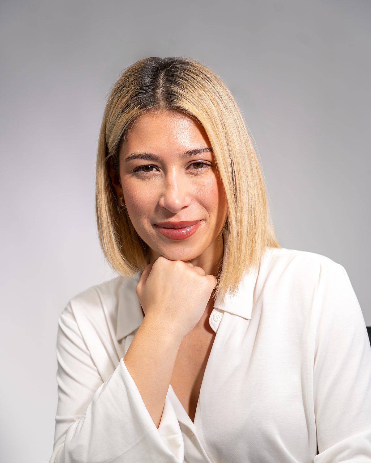 Selin Yilmaz im weißen Hemd, die Hand am Kinn, lächelnd